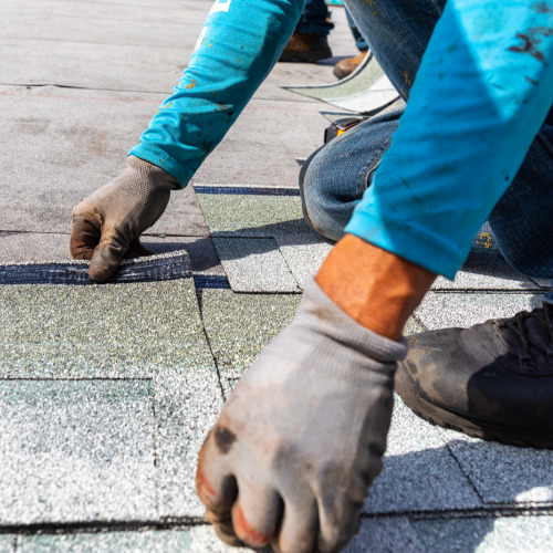 image of worker with gray gloves and blue shirt laying a shingle