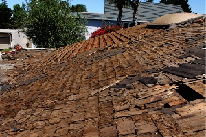 A severely damaged shingle roof with missing sections and exposed wooden battens, indicative of extensive wear or storm damage.