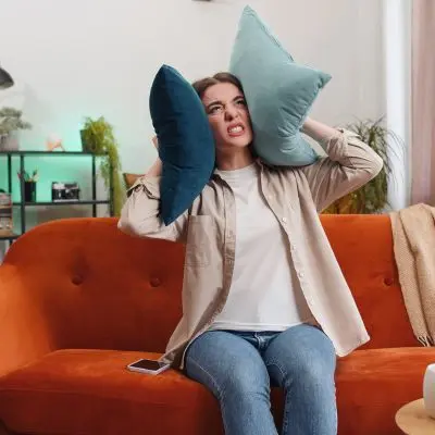 Stressed woman on sofa with pillows covering her ears.