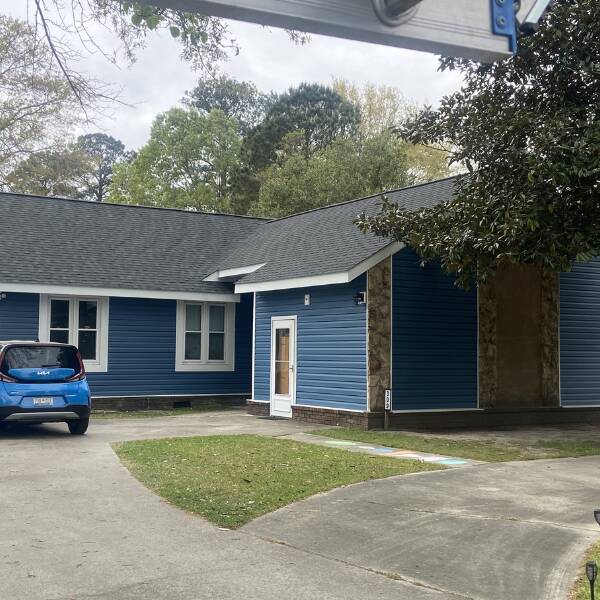 Blue single-story building with white trim and a glass-paneled door; a blue hatchback parked on a concrete driveway.
